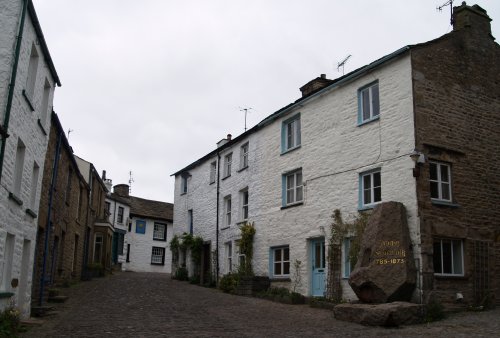 The main street of Dent Village with the Sun Inn at the top and on the right is a memorial stone to Adam Sedgwick (1785-1873) the great pioneering geologist