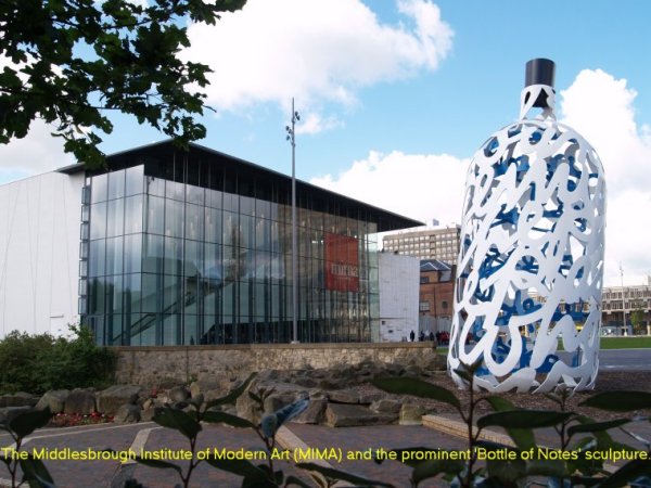 Location 00a: In the town hall square is The Middlesbrough Institute of Modern Art (MIMA) and the prominent 'Bottle of Notes' sculpture. The 'bottle' pays tribute to Middlesbrough's most famous son, Captain James Cook and the technical and engineering fabrication heritage of Teesside. The sculpture is the work of Claes Oldenburg and Coosje van Bruggen. It consists of writing in steel and the outer white shell is made up of extracts from Captain Cook's journals.