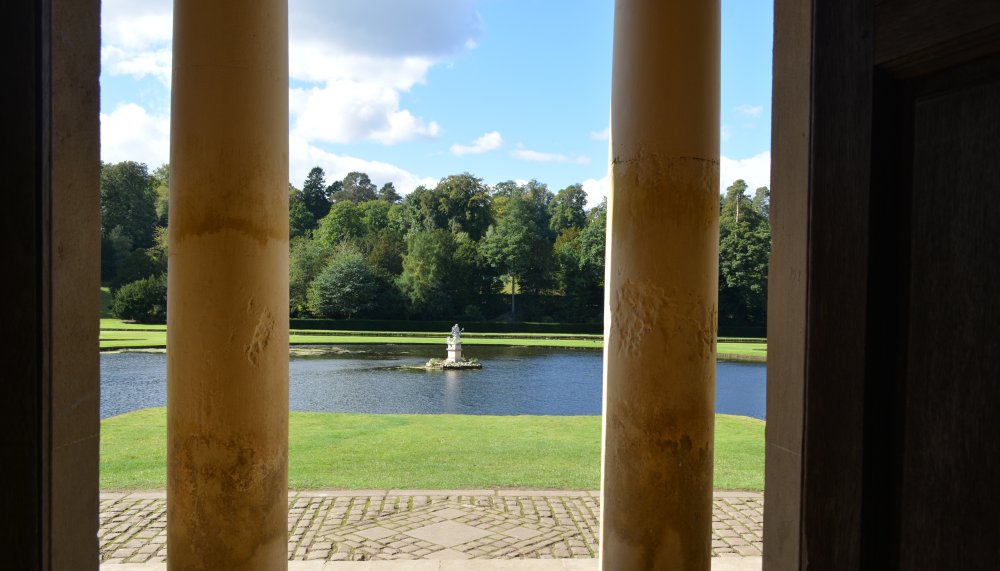 Looking through the Doric column facade of the Temple of Piety at the sculpture of Neptune in the Moon Pond Studley Royal parks and gardens